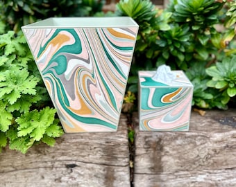 May include: A green, gold, and pink marbled wastebasket and tissue box set. The wastebasket is tall and has a square base. The tissue box is smaller and has a rectangular shape.