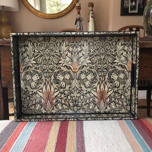 May include: A black tray with a decorative floral pattern in shades of cream, brown, and red. The tray has a black frame and a handle on the side.