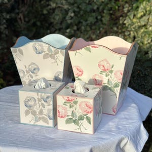 May include: Two tissue box covers and two decorative boxes with a floral pattern. The tissue box covers are blue and pink, and the decorative boxes are blue and pink.