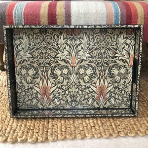 May include: A black tray with a floral pattern in shades of cream, brown, and beige. The tray is rectangular and has a raised rim.