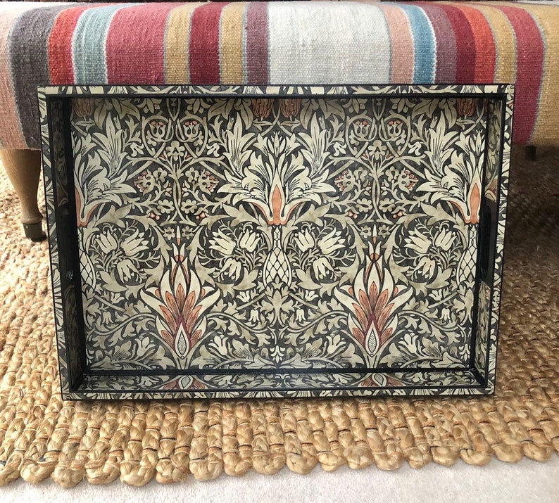 May include: A black tray with a floral pattern in shades of cream, brown, and beige. The tray is rectangular and has a raised rim.