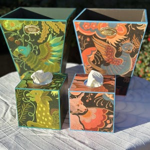 May include: Four decorative tissue box covers and two matching wastebaskets. The boxes and wastebaskets feature colorful illustrations of mythical creatures and floral patterns on a dark background. The edges are trimmed in teal.