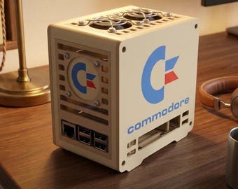 Peut inclure: Un boîtier d'ordinateur cubique beige arborant le logo Commodore en bleu et rouge. Le panneau supérieur comprend deux ventilateurs circulaires avec des grilles argentées. La façade présente un port réseau et trois ports USB, avec le mot commodore.