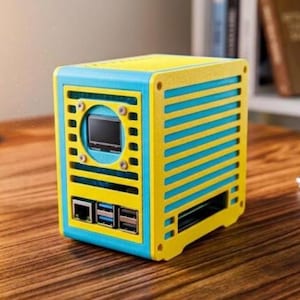 May include: A small, rectangular computer case featuring a bright yellow and light blue colour scheme. The front panel includes a circular cutout with a small black screen, and a lower section with an Ethernet port and two USB ports visible.
