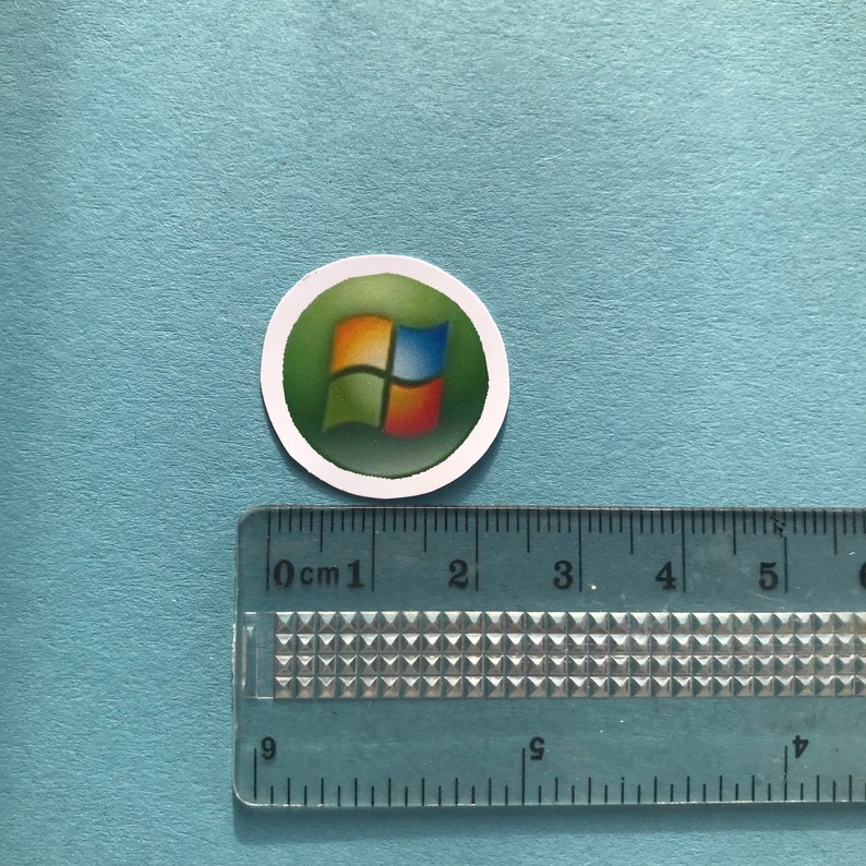 Puede incluir: Una pegatina redonda con fondo verde y el logotipo de Windows en el centro. El logotipo es una ventana de cuatro paneles con colores azul, verde y naranja.