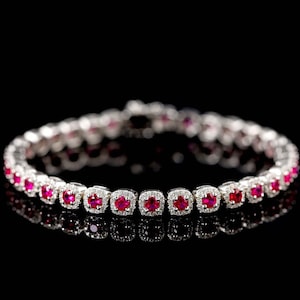 May include: A silver bracelet with a row of red ruby stones set in a square shape with a halo of smaller diamonds around each stone.