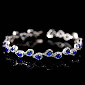 May include: A silver bracelet with a row of teardrop-shaped blue gemstones set in a silver band.