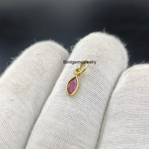 Op de afbeelding: Een kleine, traanvormige hanger met een rode edelsteen gezet in goud.