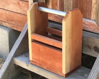 May include: A wooden crate with a metal handle, designed to hold six bottles. The crate is stained a reddish brown color and has a natural wood finish on the sides.
