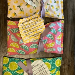 May include: Three lavender eye pillows with lemon print fabric. The pillows are tied with gray ribbon and have a tag that says "Lavender Eye Pillow" with instructions for use. The tag also says "Made with Organic Lavender Buds and Essential Lavender Oil."  "NATURALSIMPLECRAZY ON ETSY"