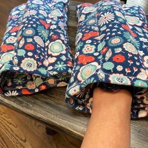 May include: Two blue floral fabric hand warmers with a white and red floral pattern. The hand warmers are filled with rice and can be heated in the microwave.
