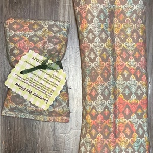 May include: Two lavender eye pillows with a floral pattern. The smaller pillow is on the left and has a tag that reads "Lavender Eye Pillow" and "NATURALS ON ETSY LECRAZY". The larger pillow is on the right and is a long, rectangular shape.