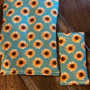 May include: Two teal blue fabric heat packs with a sunflower pattern. The larger heat pack is rectangular and the smaller heat pack is a rectangle.