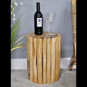 May include: A round wooden side table made of stacked logs. The table is light brown and has a natural wood finish. A wine bottle and wine glass are on top of the table.