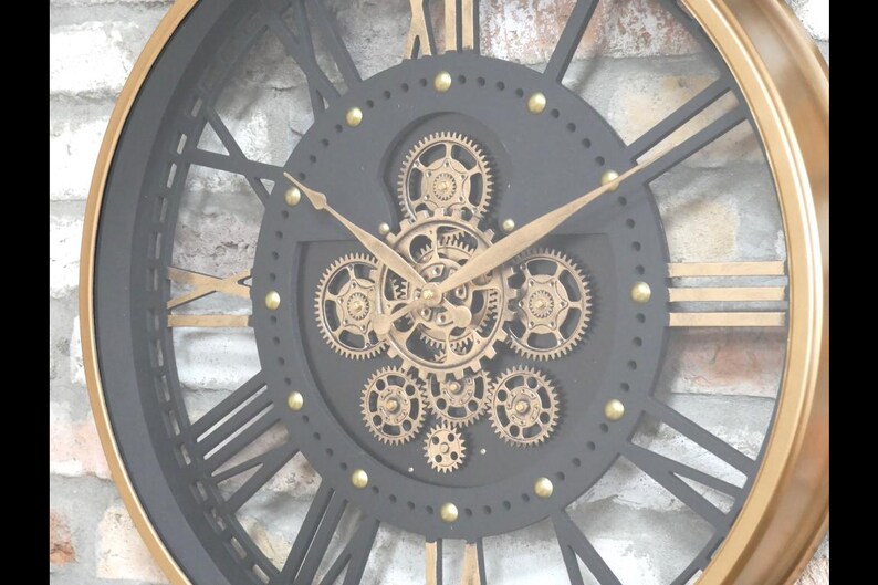 May include: A large, round wall clock with a black face and gold accents. The clock features Roman numerals, gold hands, and visible gears in the center. The outer rim is gold, and the clock has a vintage, industrial design.