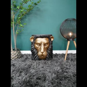 May include: A striking lion head sculpture, featuring a gold-coloured face and a black mane. This decorative piece could be a side table or stool, adding a touch of grandeur to any room. The lion's face is intricately detailed, creating a regal aesthetic.