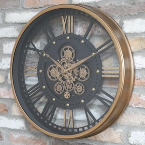 May include: A large, round wall clock with a black face and gold Roman numerals and hands. The clock features visible gears and a gold frame. The clock is mounted on a brick wall.