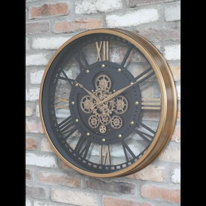 May include: A large, round wall clock with a gold-colored frame and black face. The clock features Roman numerals and visible gears in the center. The clock is mounted on a brick wall, creating a vintage, industrial aesthetic.