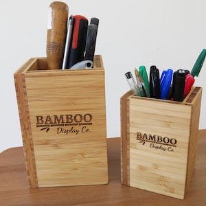 Peut inclure: Deux porte-crayons en bambou avec le logo "BAMBOO Display Co." gravé sur le devant. Le plus grand porte-crayons contient des outils, tandis que le plus petit contient des stylos.