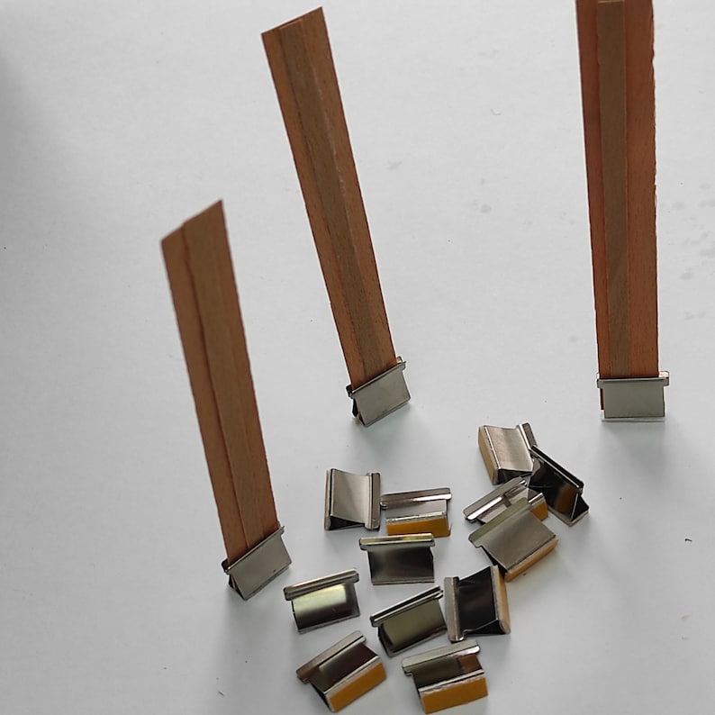 May include: A set of wooden candle wicks with metal clips. The wicks are brown and the clips are silver.