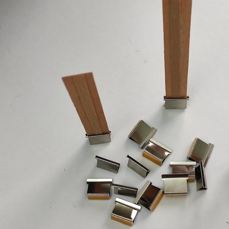 May include: Two wooden candle wicks with metal holders, and a pile of metal candle wick holders. The holders are silver and have a slight shine.