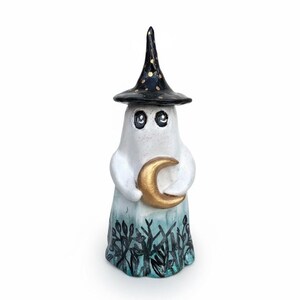 May include: A ceramic ghost figure wearing a black witch's hat with gold spots. The ghost holds a gold crescent moon. The base is painted teal and black. A Halloween decoration.