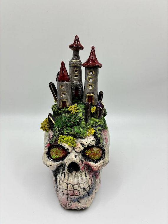 A hand-painted skull transformed into a miniature gothic kingdom complete with tiny towers and crystals — absurdly detailed desk sculpture.