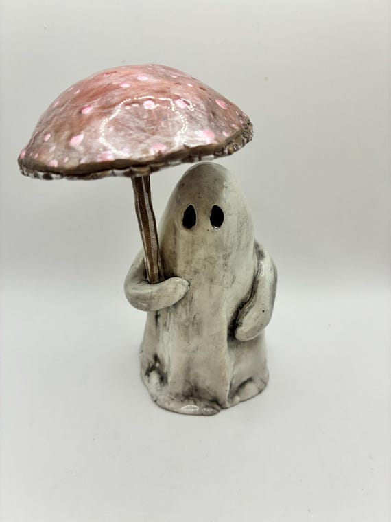 A tiny polymer clay ghost holding a mushroom umbrella — the kind of hyper-specific whimsy that makes you smile and immediately want to put it on your desk.