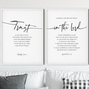 May include: Two white framed prints with black text on a white background. The left print says "Trust in the Lord with all your heart and lean not on your own understanding. In all your ways submit to him, and he will make your paths straight. Proverbs 3:5-6". The right print says "Blessed is the one who trusts in the Lord whose confidence is in him. They will be like a tree planted by the water that sends out its roots by the stream. It does not fear when heat comes. Its leaves are always green. It has no worries in a year of drought and never fails to bear fruit. Jeremiah 17:7-8".