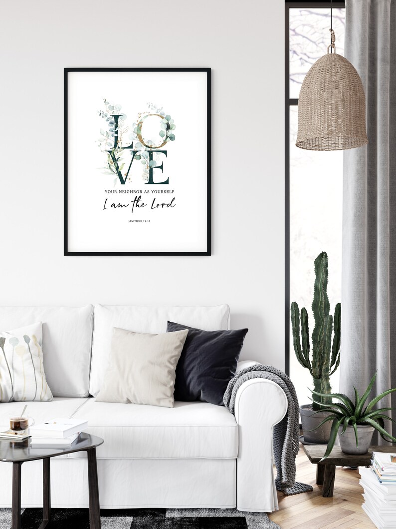 Op de afbeelding: Een zwart ingelijst print met een witte achtergrond waarop het woord "LOVE" in grote letters staat met groene en gouden bloemmotieven. De tekst "Your neighbor as yourself I am the Lord" staat onder het woord "LOVE" met de bijbelverwijzing "Leviticus 19:18" eronder.