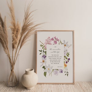 May include: A white printable art print with a floral border and a quote from the Bible: "I am the resurrection and the life. The one who believes in me will live, even though they die. And whoever lives by believing in me will never die." John 11:25-26