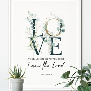 Op de afbeelding: Een witte ingelijste print met een groen en gouden bloemendesign dat het woord "LOVE" spelt. De tekst "Your neighbor as yourself I am the Lord" staat onder het bloemendesign, met de bijbelverwijzing "Leviticus 19:18" eronder.