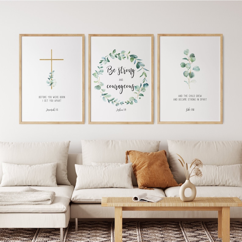 May include: Three framed prints with inspirational quotes and watercolor greenery. The first print features a gold cross with the text "Before you were born I set you apart Jeremiah 1:5". The second print features a wreath of green leaves with the text "Be strong and courageous Joshua 1:9". The third print features a sprig of green leaves with the text "And the child grew and became strong in spirit Luke 2:40".