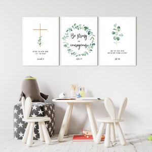 May include: Three framed prints with white backgrounds and green foliage designs. The first print features a gold cross with the text "BEFORE YOU WERE BORN I SET YOU APART Jeremiah 1:5". The second print features a wreath of green leaves with the text "Be strong and courageous Joshua 1:9". The third print features a sprig of green leaves with the text "AND THE CHILD GREW AND BECAME STRONG IN SPIRIT Luke 1:80".