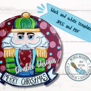May include: A red, white, and blue Christmas door hanger featuring a nutcracker with a green hat and a white beard. The text "Merry Christmas" is written on a white banner below the nutcracker.