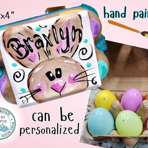 May include: Hand-painted wooden egg carton with a bunny design and the name "Braxlyn" on the front. The carton is 6 inches by 4 inches and can be personalized. The carton is shown with six colorful plastic eggs inside.