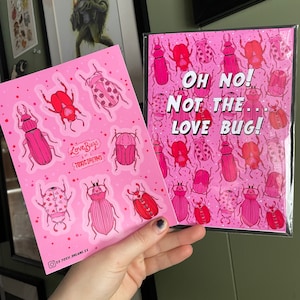 May include: Pink sticker sheet with a set of 8 love bug illustrations. The sticker sheet has the text "Love Bugs Say It With Toxic Dreams". A pink card with a repeating pattern of love bugs and the text "Oh No! Not the Love Bug!" is in the background.