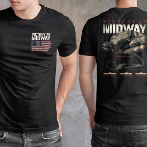May include: Black t-shirt with the text "Victory at Midway" and a distressed American flag graphic on the front. The back features an illustration of a plane and text related to the Battle of Midway.