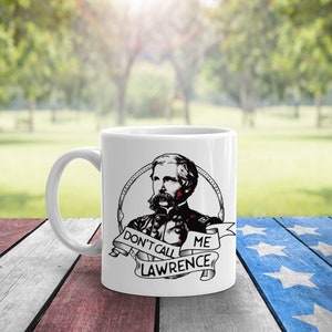 May include: White ceramic mug with a black and white illustration of a man with a mustache and beard. The man is wearing a military uniform and holding a gun. The text "Don't call me Lawrence!" is written on a banner below the illustration.