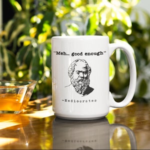 May include: White ceramic coffee mug with a black and white illustration of a man with a beard and the text "Meh... good enough" - Mediocrates.