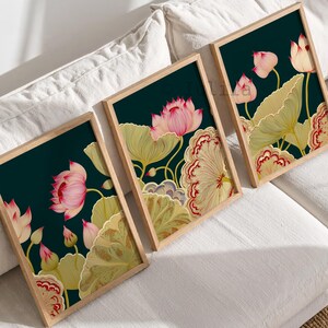 May include: Three rectangular wall art prints in light wood frames, each featuring a dark teal background with illustrations of pink lotus flowers, green lily pads, and decorative scalloped edges in shades of cream and deep red.