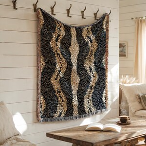 Peut inclure: Une couverture tiss&eacute;e avec un motif r&eacute;p&eacute;t&eacute; de cercles bleu fonc&eacute; et beige et de rayures verticales. La couverture est frang&eacute;e en bas et est accroch&eacute;e &agrave; un mur blanc. La couverture mesure environ 152 cm de large et 178 cm de long.