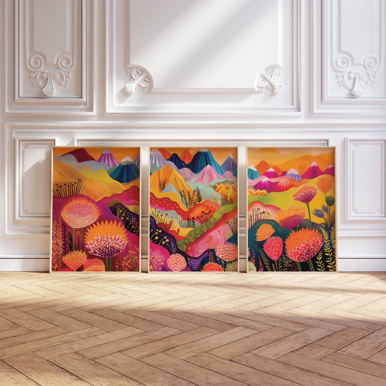 Funky floral triptych displayed in three framed panels against an elegant light wall with decorative molding. The artwork combines bright orange, pink, yellow and deep blue landscape shapes with oversized botanical forms and abstract mountains, creating colorful statement wall art for maximalist, eclectic and dopamine-inspired interiors.