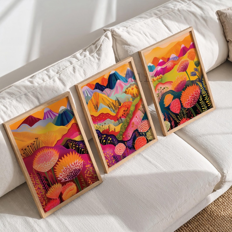 Colorful 3 piece wall art displayed in natural wood frames on soft neutral bedding. The vibrant triptych features abstract mountains, bold orange and pink flowers, layered landscape shapes and rich yellow, magenta and blue tones, creating playful maximalist wall decor for bedrooms, living rooms and colorful contemporary interiors.