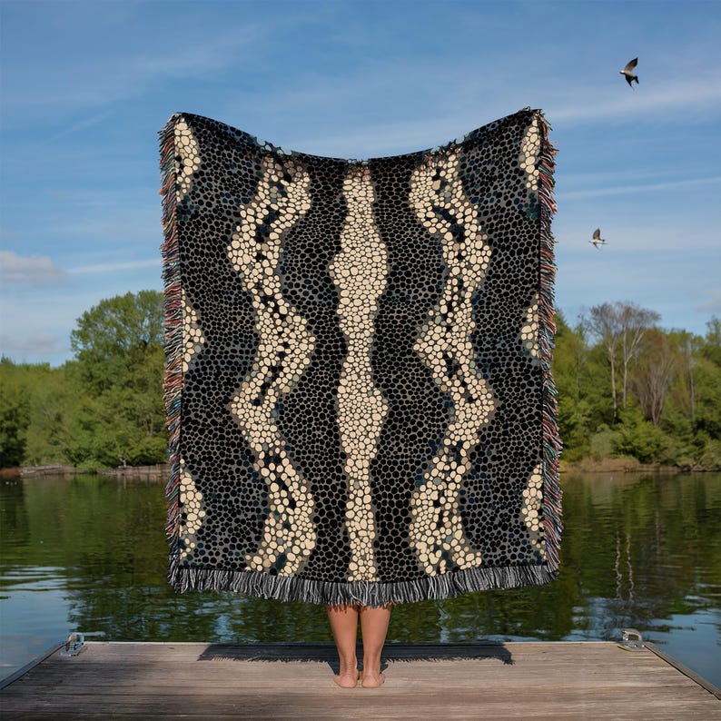 Peut inclure: Une grande couverture &agrave; motifs avec un design noir et cr&egrave;me, tenue contre un ciel bleu et un lac. La couverture pr&eacute;sente un motif r&eacute;p&eacute;titif de petits cercles et un bord &agrave; franges. Le motif est sym&eacute;trique, avec une bande centrale cr&egrave;me.