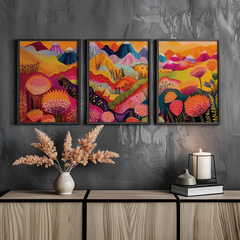 Colorful floral wall art set of 3 displayed in black frames above a dark console against a charcoal wall. The vivid orange, pink, yellow and blue artwork creates strong contrast with the moody interior, making the abstract botanical triptych a bold focal point for modern maximalist spaces.