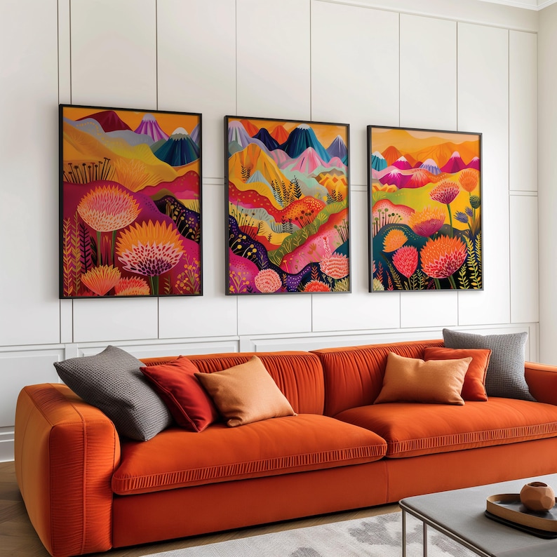 Maximalist gallery wall set displayed in black frames above a bold orange sofa. The three prints combine vivid floral forms, abstract mountains and layered landscape shapes in pink, orange, yellow and blue, creating energetic funky wall art for colorful living rooms and eclectic contemporary interiors.