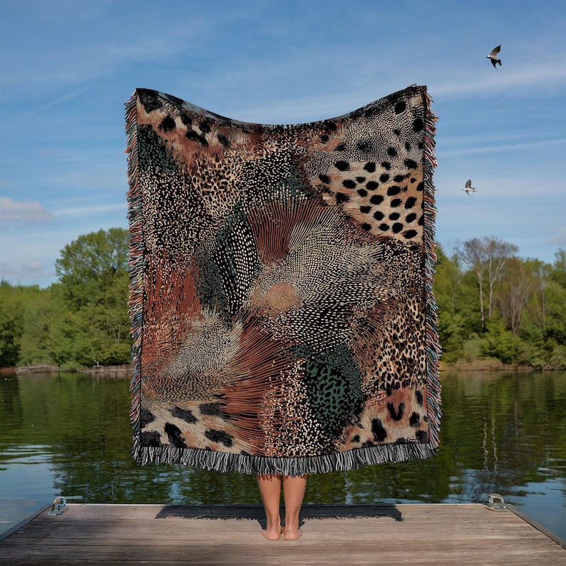 Op de afbeelding: Een rechthoekige geweven plaid met een complex, meerkleurig dierenprintpatroon met luipaardvlekken, jachtluipaardstippen en abstracte texturen in tinten zwart, bruin, beige en groen, afgewerkt met een franjerand aan alle zijden.
