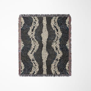 Peut inclure: Une couverture tiss&eacute;e avec un motif r&eacute;p&eacute;titif de points bleu fonc&eacute; et blanc cass&eacute;. Des rayures verticales ondul&eacute;es de points blanc cass&eacute; et une bande centrale de la m&ecirc;me couleur sont pr&eacute;sentes. La couverture a une bordure &agrave; franges.