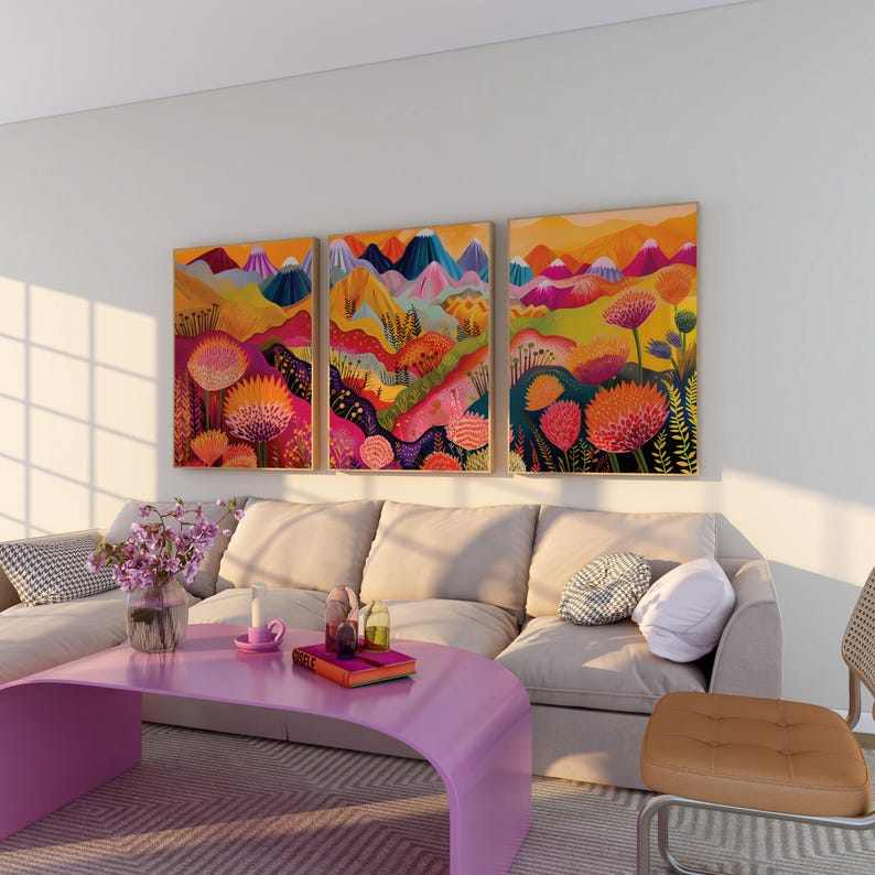 Bold floral triptych displayed above a light sectional sofa with a lavender coffee table. The colorful framed prints feature orange, magenta, yellow and deep blue abstract landscape forms with oversized botanical shapes, creating vibrant statement wall art for playful living rooms, eclectic interiors and dopamine decor.